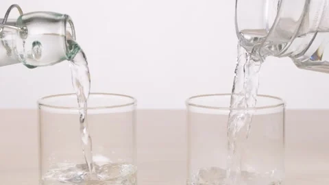 Pouring Water Into Two Glasses on a Tabletop Stock Footage 320031918