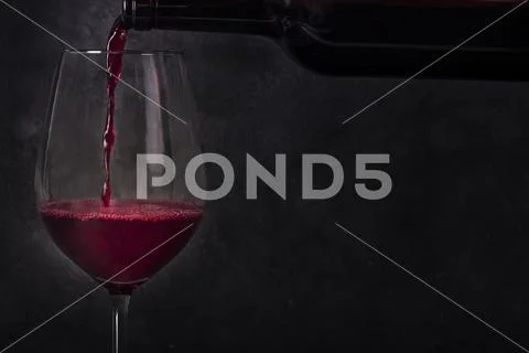 Pouring wine into a glass from a bottle, side view on a black background with a Stock Photos