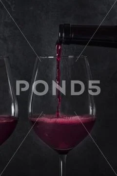 Pouring wine into glasses from a bottle, close-up on a dark background Stock Photos