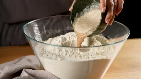 Pouring yeast mixture over the flour in a glass bowl in slow motion 4K Stock Footage 266153036