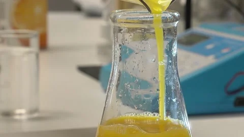 Pouring a yellow liquid into a flask from a test tube- 库存影片 147908020