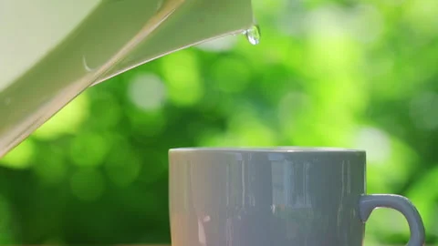 Pours hot water into a cup on a table in a garden landscape 스톡 동영상 212970557