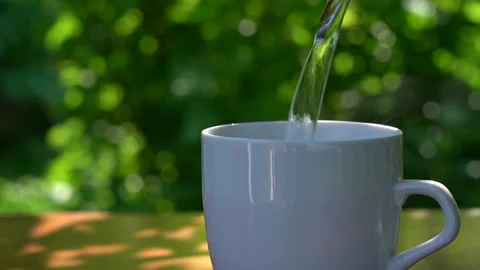 Pours hot water into a cup on a table in a garden landscape Stock-Footage 223692848