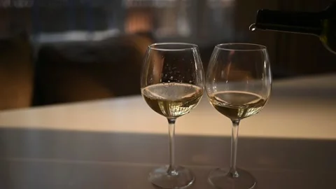 Pours white dry wine into a one of two glasses standing on white table Stock Footage 152521745