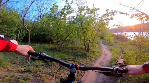 POV - cyclist rides into the sunset on a forest trail along the river. Stock Footage 129695435