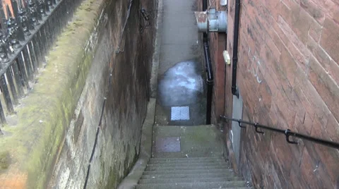 POV down stone steps into back alley with red sand stone buildings Stock Footage 35833314