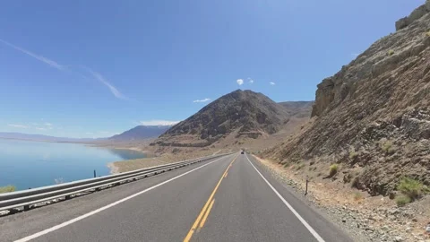 POV driving between a steep rocky mountain and bright blue desert lake Vídeos de archivo 334625484