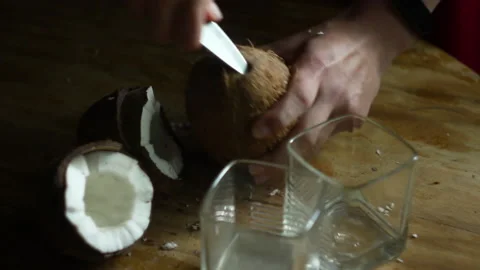 POV female hands using knife to open coconut and puring coconut water into glass Video stock 131272772