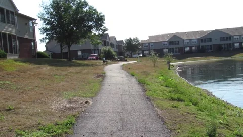 POV forward tracking shot on sidewalk between pond and apartment buildings Stock Footage 201500561