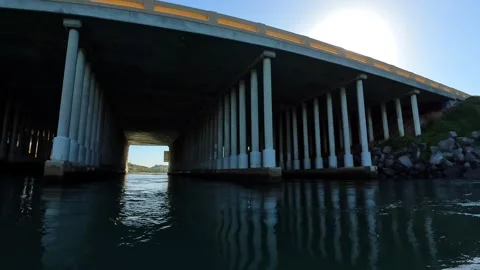 POV gliding under concrete bridge pillars Carlsbad Lagoon sunny day Stock Footage 331765854