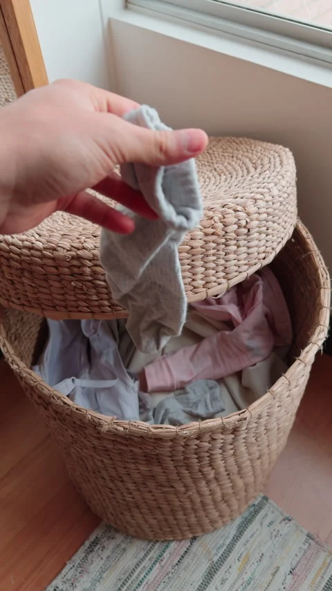 POV of hand placing dirty socks into woven laundry basket Stock Footage 316549048