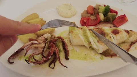 POV hands cutting grilled squid, potatoes and vegetables, restaurant table Stock Footage 321193235
