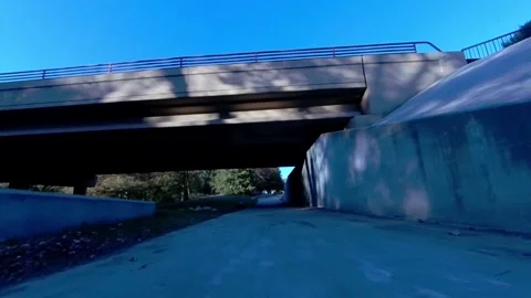 POV jogging on concrete path, going under street overpass, sunny fall day Vidéo 272713729