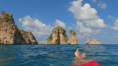 Pov of legs relaxing while floating on sea with faraglioni in background Stock Footage 279860009