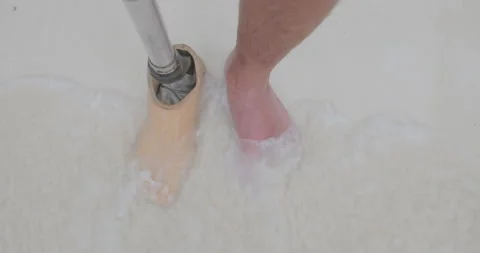 POV man with artificial bionic legs standing on sandy beach feet touch sea wave. Stock Footage 195000268