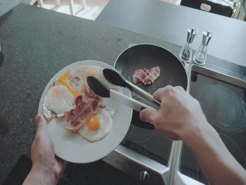 POV of a man cooking breakfast eggs and bacon in a pan Stock Footage