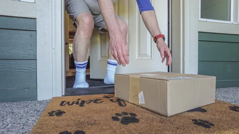 POV of Man Opening Front Door to Pick Up Cardboard Package From Doormat 库存影片 334687226