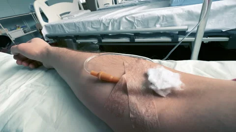 POV of a man's arm with an IV needle in the median cubital vein in a clinic ward Stock Footage 260854579