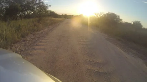 POV from the nose of a vehicle driving along a dirt road then onto tar road in Stock Footage