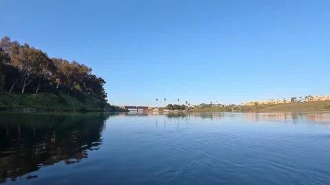 POV passing under bridge pillars into calm Carlsbad Lagoon water clear blue sky Stock Footage 331765862