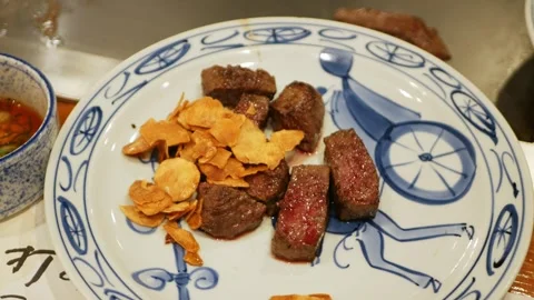 Pov to a plate full of Kobe steak grilled cutted with golden fried garlic p.. Видео 335579680
