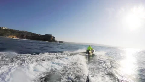POV of pro surfer being dragged behind jet ski on surfing board during sunny day Stock Footage 163044062
