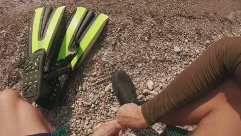 POV shot, guy puts on diving boots, takes fins in his hand and goes into sea Stock Footage 252208159