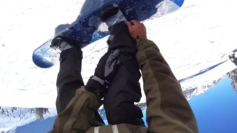 POV of a snowboarder buckling into his bindings on his snowboard and putting on Stock Footage
