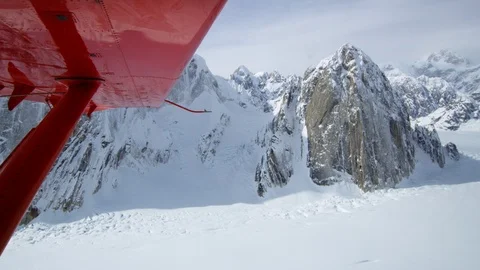 POV of snowy Alaskan mountains from inside a small red airplane, visible wing Stock Footage 129129758