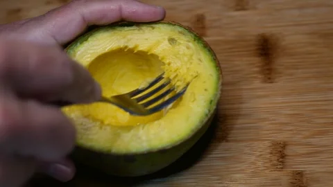 POV: Someone mashing an avocado with a fork. Avocado mashed in its own peel Stock Footage 320139264