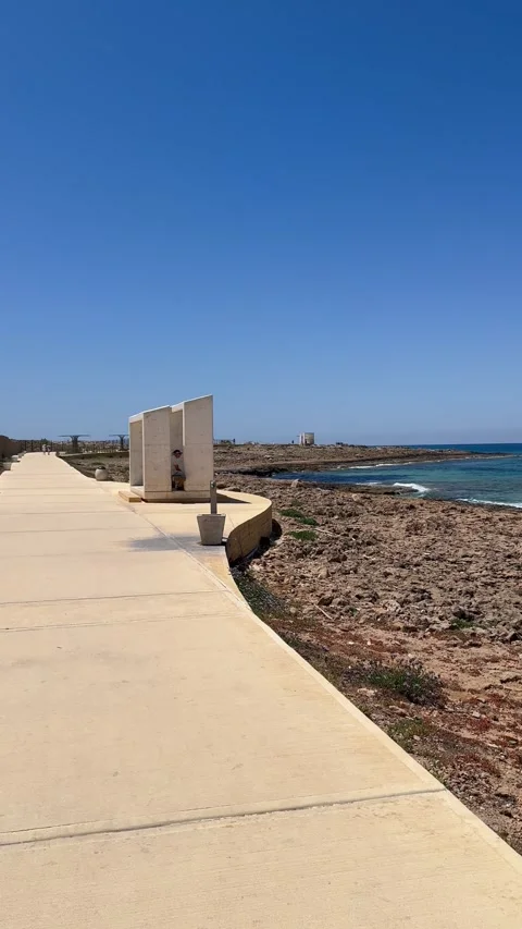 POV tracking shot walking along a white concrete coastal path near a rocky sea Stock Footage 336320537