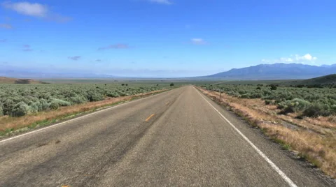 POV- Two lane road past sage juniper plain toward distant mountain Stock Footage 64631653