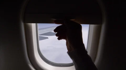 POV: Unknown person pulls up airplane window shade and reveals bright blue sky. Stock Footage