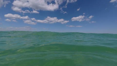 POV view floating in open sea, calm green waves under bright blue sky with Stock Footage 316310910
