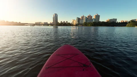 POV View: Paddleboarding on Calm River Towards Modern City Skyline at Sunset Stock Footage 340114451