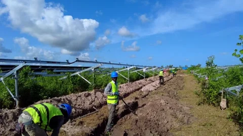 POV walking past workers in safety gear digging trenches at solar farm with 스톡 동영상 332825441