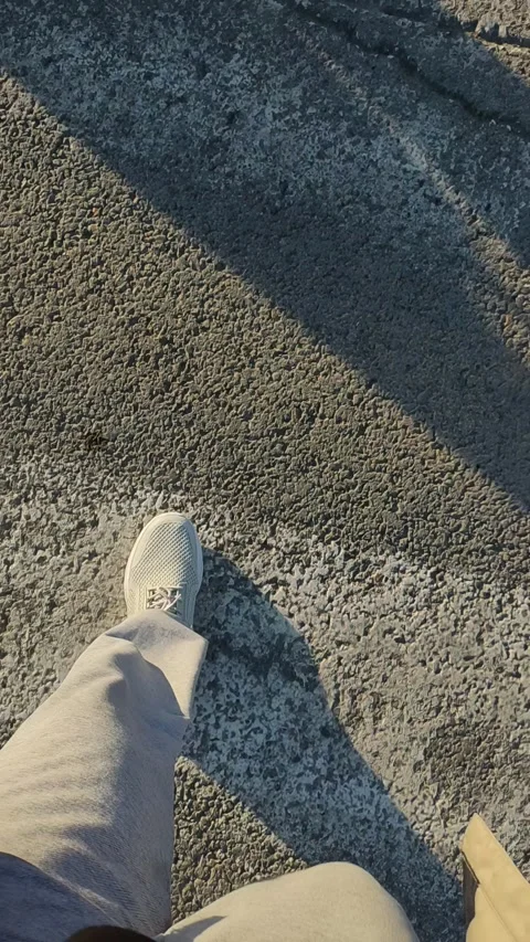POV walking on rough asphalt surface, long shadows, white sneakers Stock Footage 333471936