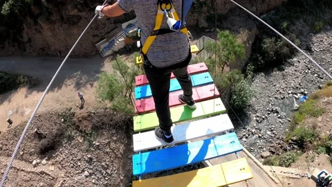 POV walking on a suspension bridge with colored steps over a river in highlands Stock-Footage 198764391