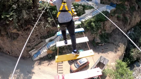 POV walking on a suspension bridge with colored steps over a river in highlands 库存影片 198764699