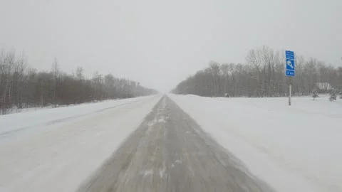 POV while driving along a snow covered surrounded by trees road during snowstorm Stock Footage 297633582