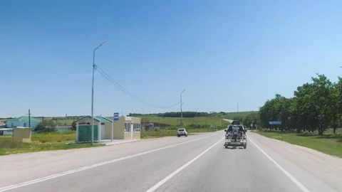 POV Windshield View of SUV Towing Motorcycle Trailer Passing Rural Buildings Vídeo Stock 338277373