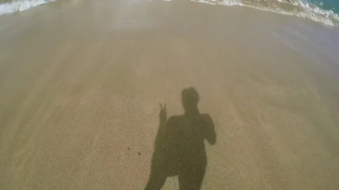 POV Of Young Woman's Shadow Walking Toward Ocean, She Holds Up A Peace Sign Vídeos de archivo 74111768