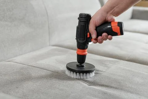 Power drill brush cleaning sofa upholstery for deep fabric stain removal Stock Photos