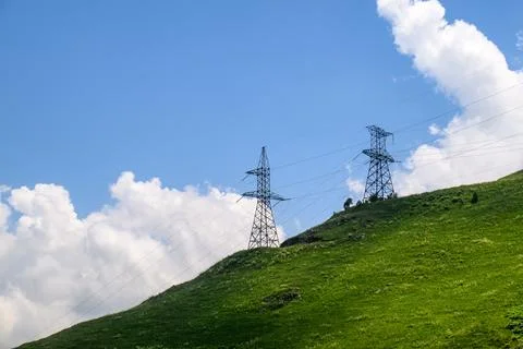 Power infrastructure on rolling green hillside against bright sky 写真素材