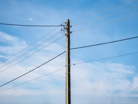 Power line going through dirt road under cloudy sky Фото