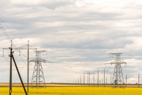 Power line in rape field. A line of electric poles with cables of electricity Stock Photos