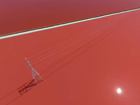 Power lines extending over vibrant red salt ponds in Fremont, California, w.. Stock Photos