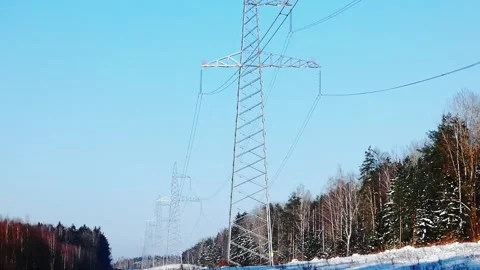 Power lines stand tall against a clear blue sky in a snowy landscape with trees Stock Footage 332015402