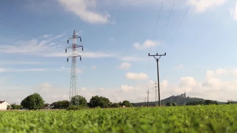 Power lines stretch across a green field toward a distant hilltop castle under a Video stock 313843651