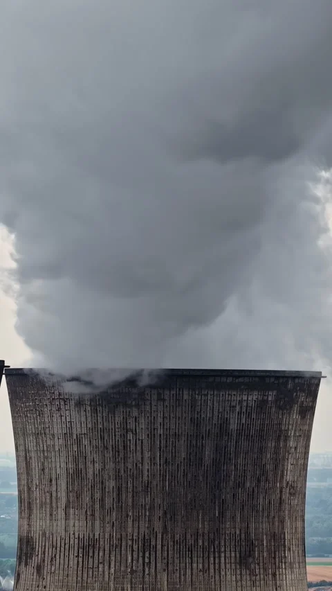 Power plant cooling tower emitting steam and smoke against a cloudy gray sky Stock Footage 344524905